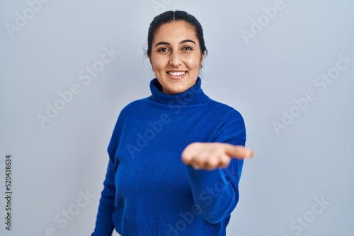 Young hispanic woman standing over isolated background smiling cheerful offering palm hand giving assistance and acceptance.