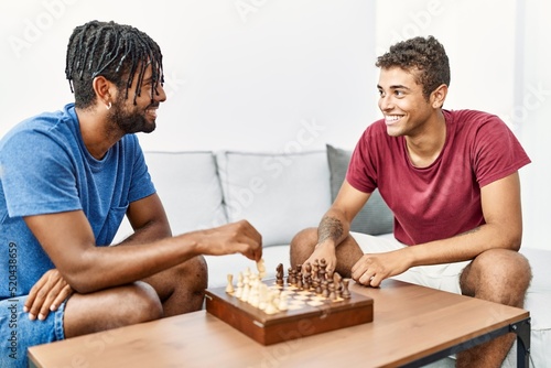 Two men friends playing chess sitting on sofa at home