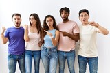 Group of young people standing together over isolated background surprised pointing with hand finger to the side, open mouth amazed expression.