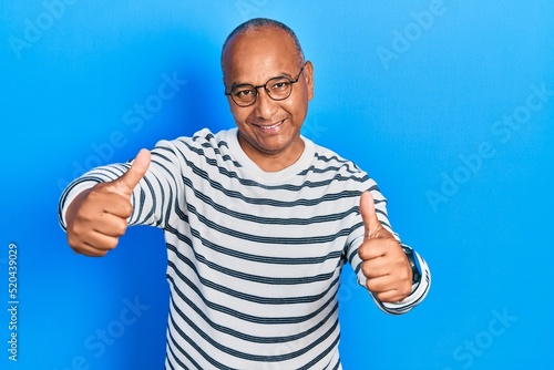 Middle age latin man wearing casual clothes and glasses approving doing positive gesture with hand, thumbs up smiling and happy for success. winner gesture.