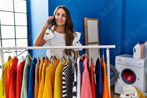 Young hispanic woman talking on the smartphone at laundry room
