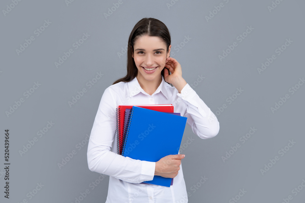 Teenager student girl isolated on grey background. Cheerful young woman student in shirt hold notebooks showing. High school university college students. Teenager student girl isolated on grey background. Cheerful young woman student in shirt hold notebooks showing. High school university college students.