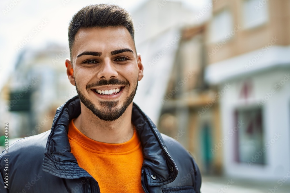 Fototapeta premium Handsome hispanic man with beard smiling happy and confident at the city wearing winter coat