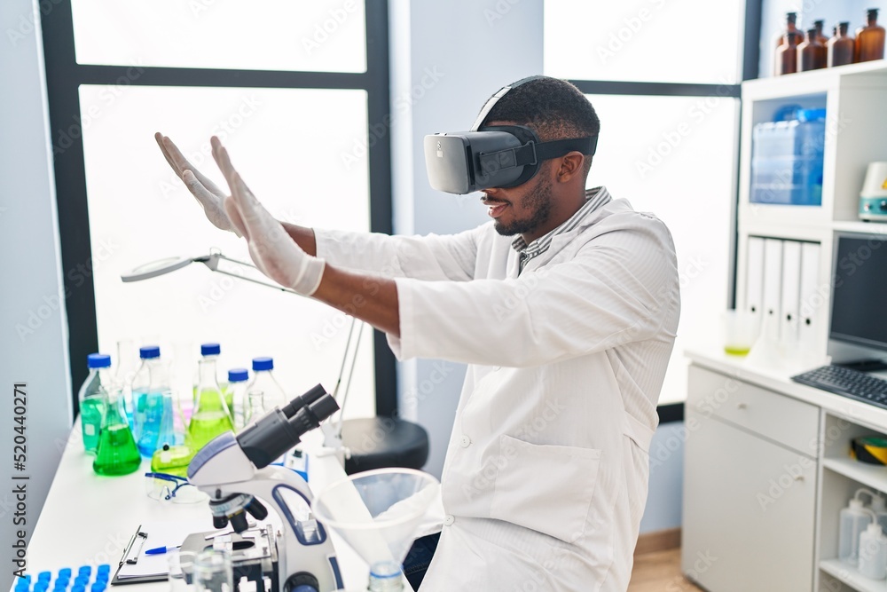 Young african american man wearing scientist uniform using virtual reality glasses at laboratory Young african american man wearing scientist uniform using virtual reality glasses at laboratory