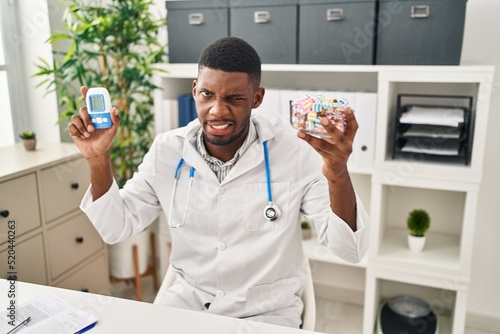 African american doctor man using glucose meter clueless and confused expression. doubt concept.
