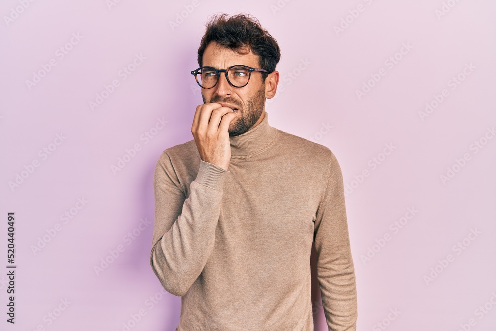 Handsome man with beard wearing turtleneck sweater and glasses looking stressed and nervous with hands on mouth biting nails. anxiety problem. Handsome man with beard wearing turtleneck sweater and glasses looking stressed and nervous with hands on mouth biting nails. anxiety problem.