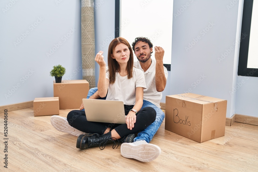 Young couple using laptop at new home doing italian gesture with hand and fingers confident expression Young couple using laptop at new home doing italian gesture with hand and fingers confident expression