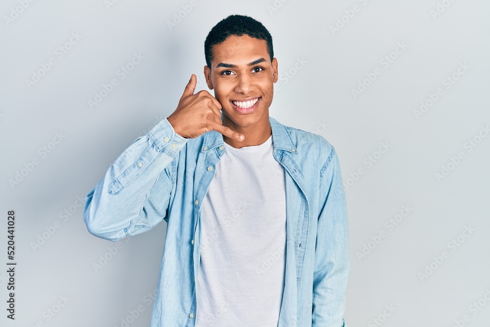 Young african american guy wearing casual clothes smiling doing phone gesture with hand and fingers like talking on the telephone. communicating concepts. Young african american guy wearing casual clothes smiling doing phone gesture with hand and fingers like talking on the telephone. communicating concepts.