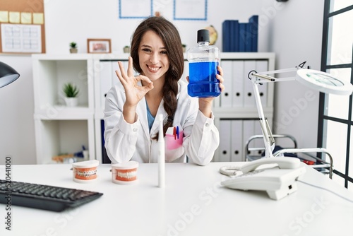 Young dentist woman holding mouthwash for fresh breath doing ok sign with fingers  smiling friendly gesturing excellent symbol