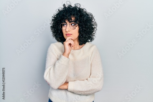 Young middle east woman wearing casual white tshirt with hand on chin thinking about question, pensive expression. smiling with thoughtful face. doubt concept.