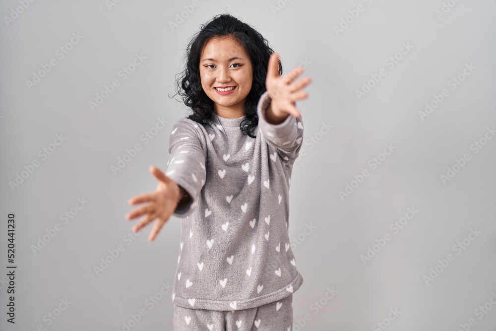 Young asian woman wearing pajama looking at the camera smiling with open arms for hug. cheerful expression embracing happiness. Young asian woman wearing pajama looking at the camera smiling with open arms for hug. cheerful expression embracing happiness.