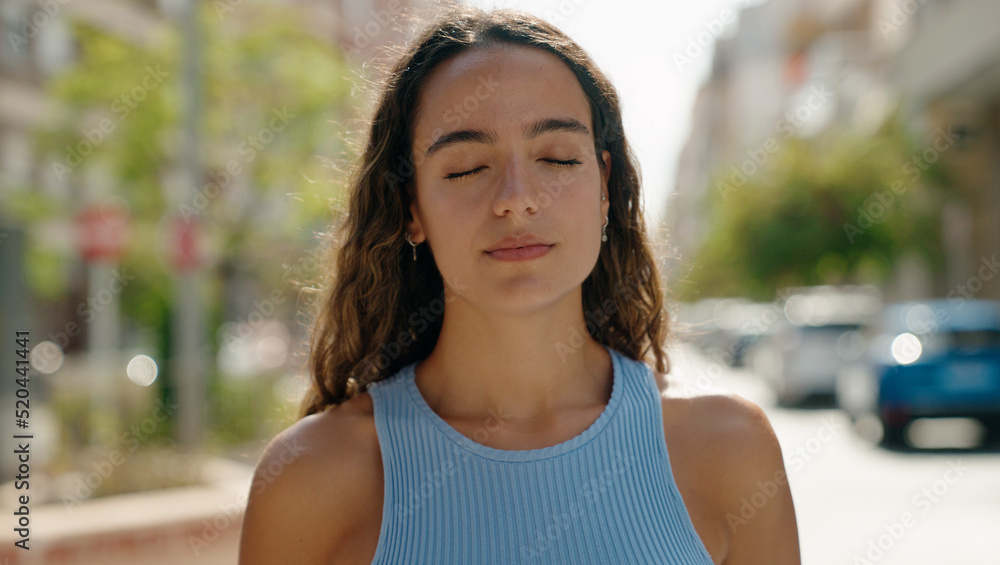 Young beautiful hispanic woman standing with serious expression and close eyes at street