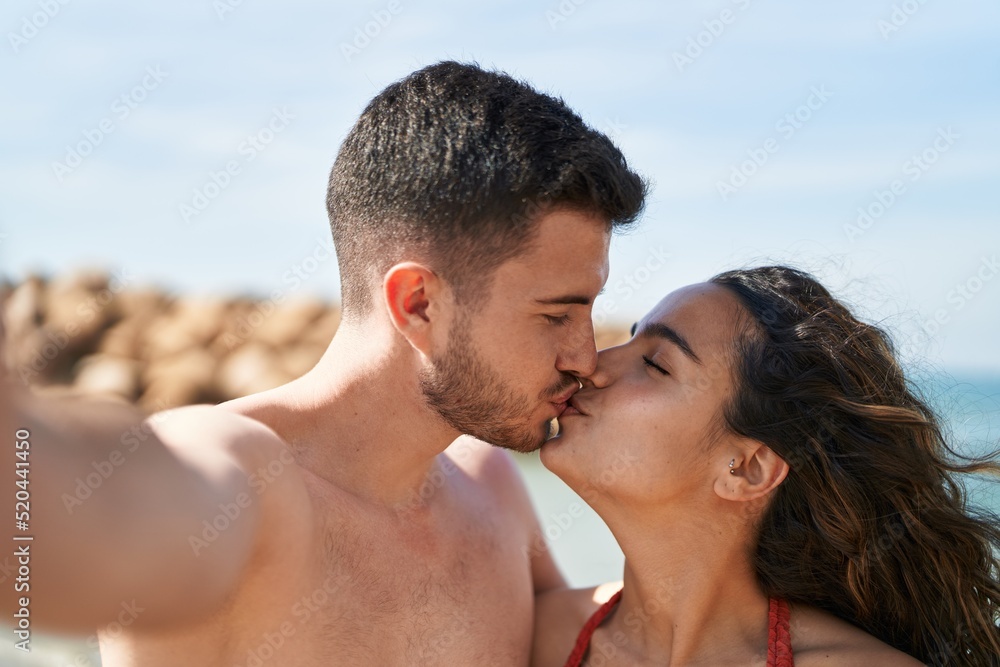 Young hispanic couple tourists wearing swimsuit make selfie by camera at seaside Young hispanic couple tourists wearing swimsuit make selfie by camera at seaside