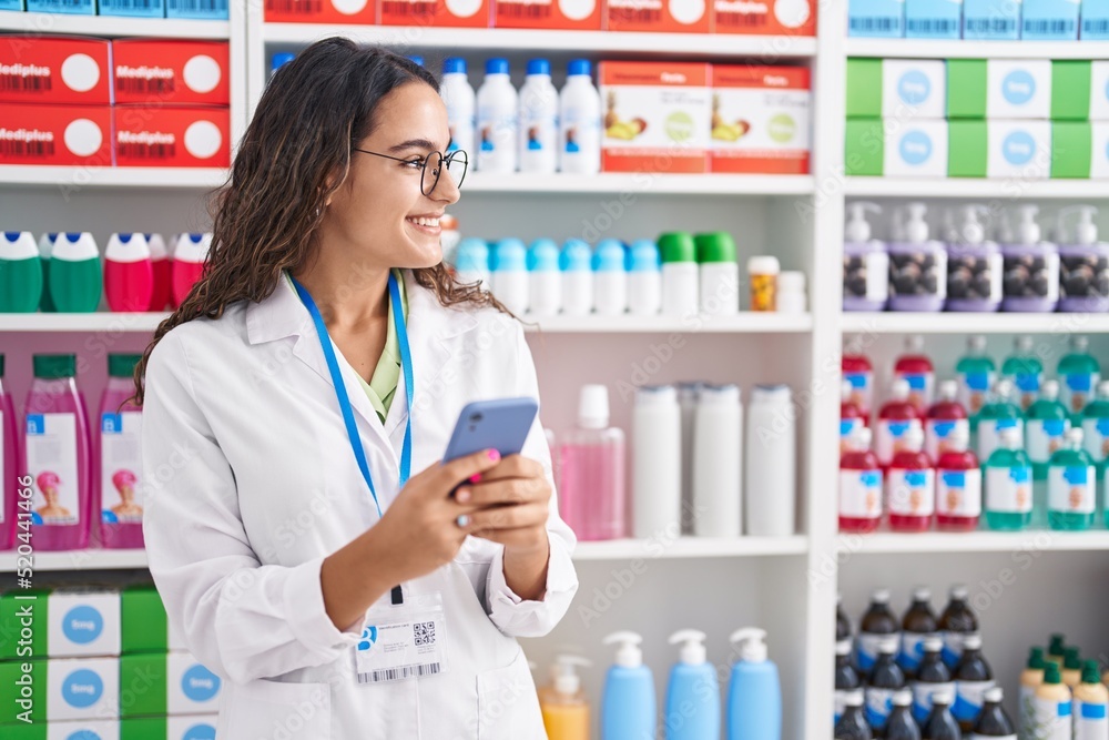 Young beautiful hispanic woman pharmacist using smartphone working at pharmacy Young beautiful hispanic woman pharmacist using smartphone working at pharmacy