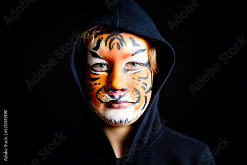 Mysterious look of a child with feline character, painted the face of a dangerous, serious tiger, isolated on black background.