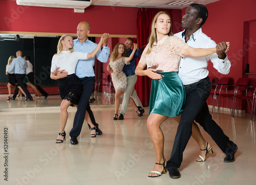 Portrait of positive adult pairs enjoying dancing salsa in modern dance studio