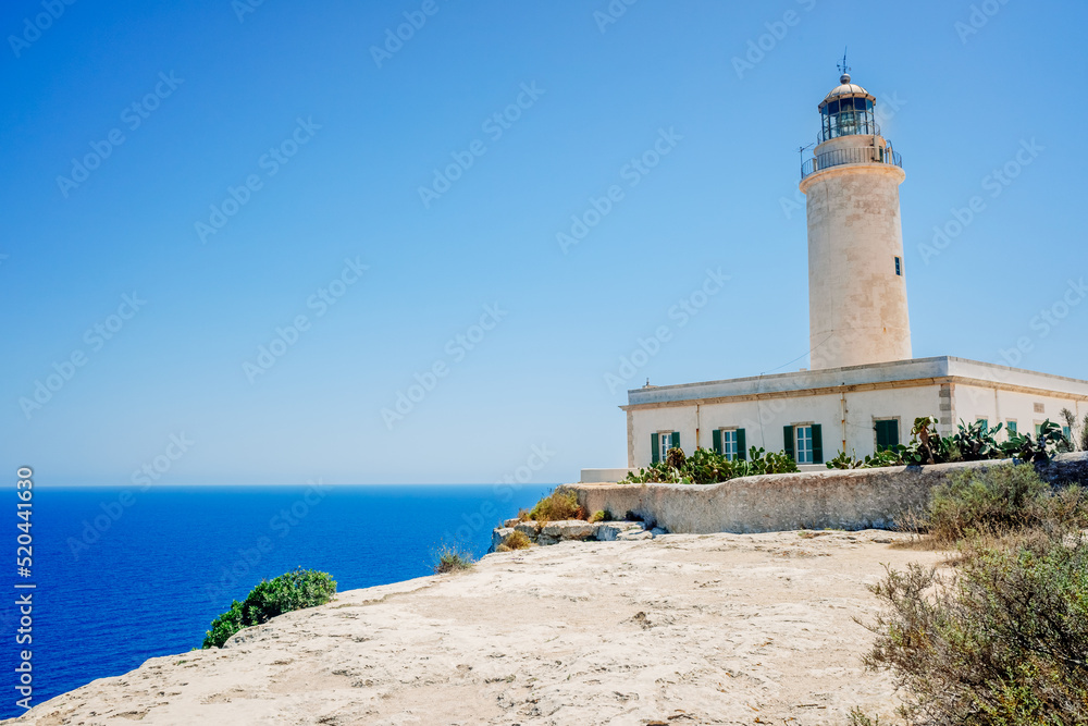 Formentera's lighthouse next to the sea cliff illuminates the coast for sailors.