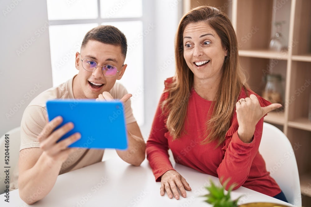 Mother and son using touchpad device pointing thumb up to the side smiling happy with open mouth Mother and son using touchpad device pointing thumb up to the side smiling happy with open mouth