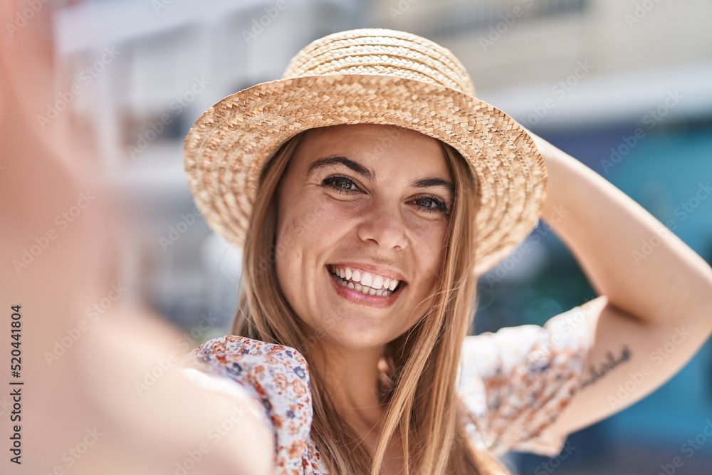Young woman tourist wearing summer hat make selfie by camera at street