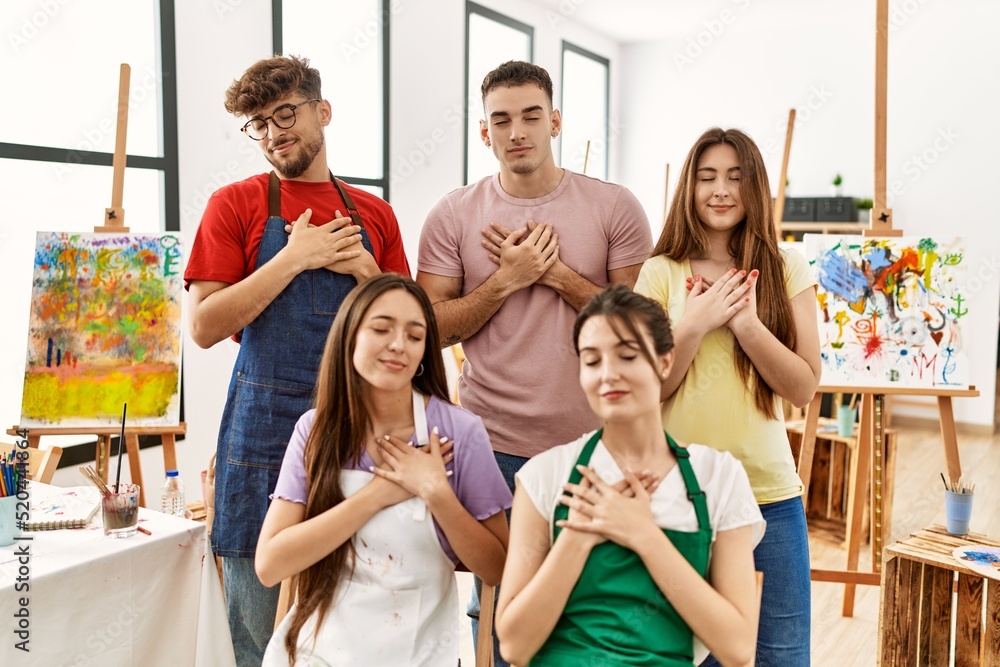 Group of five hispanic artists at art studio smiling with hands on chest with closed eyes and grateful gesture on face. health concept.