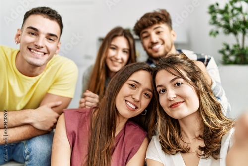 Group of young friends smiling happy make selfie by the smartphone sitting on the sofa at home.