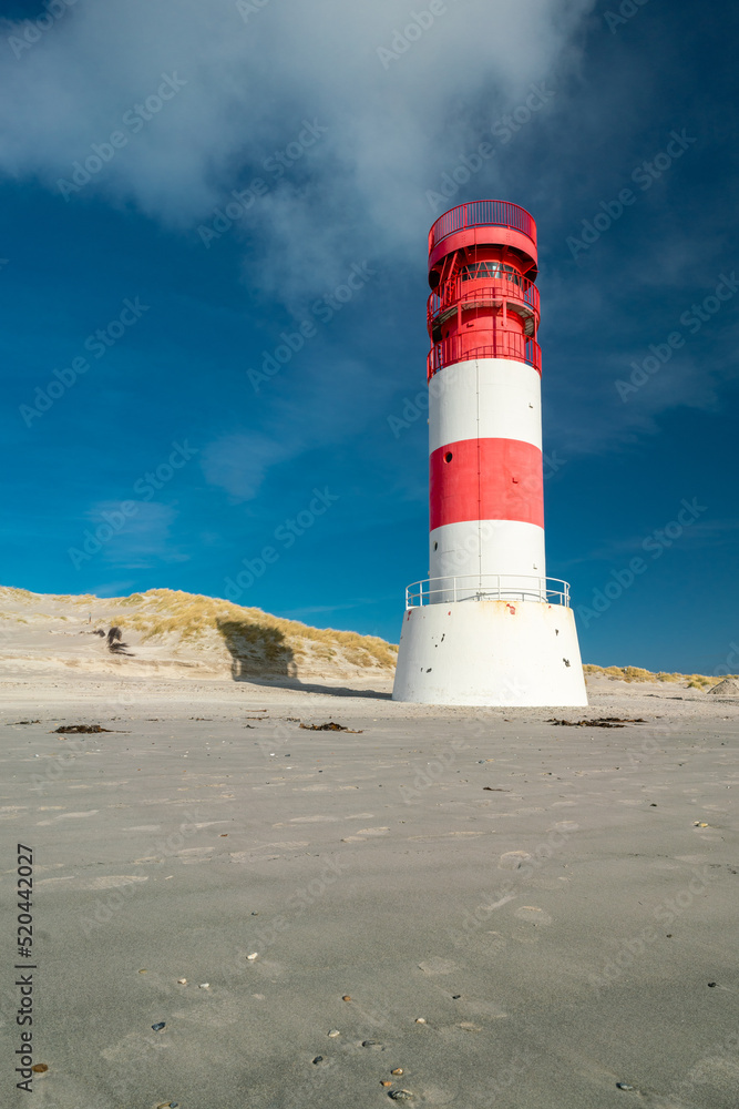 Vertical shot of small red and white lighthouse on the sandy beach of Dune island, Heligoland, on a beautiful sunny winter day with blue sky.