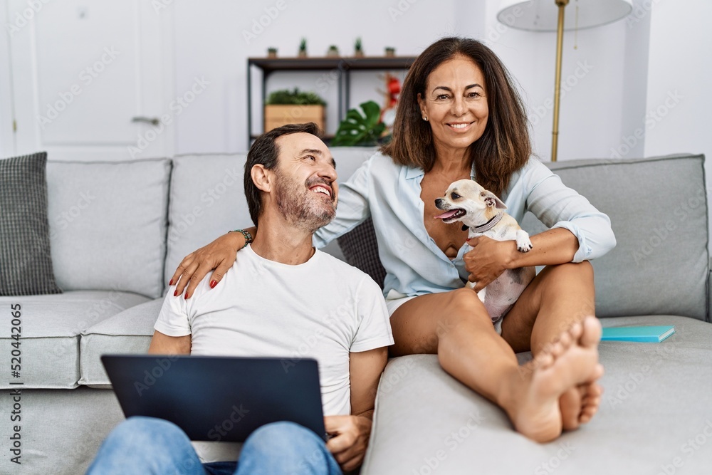 Middle age man and woman couple using laptop sitting on sofa with chihuahua at home Middle age man and woman couple using laptop sitting on sofa with chihuahua at home