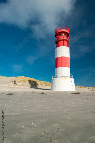 Vertical shot of small red and white lighthouse on the sandy beach of Dune island, Heligoland, on a beautiful sunny winter day with blue sky.