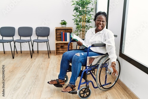 Fotobehang Young black woman sitting on wheelchair at waiting room angry and mad screaming frustrated and furious, shouting with anger