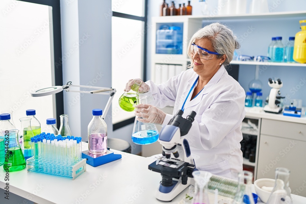 Middle age woman wearing scientist uniform pouring liquid on test tube at laboratory Middle age woman wearing scientist uniform pouring liquid on test tube at laboratory