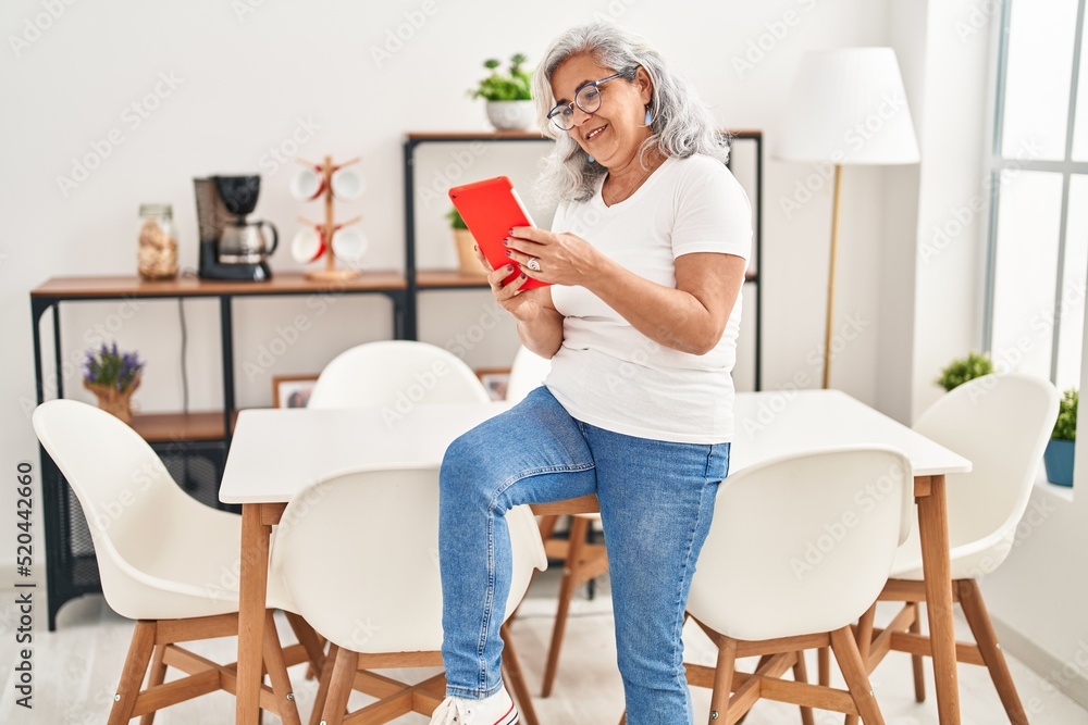 Middle age woman using touchpad sitting on table at home