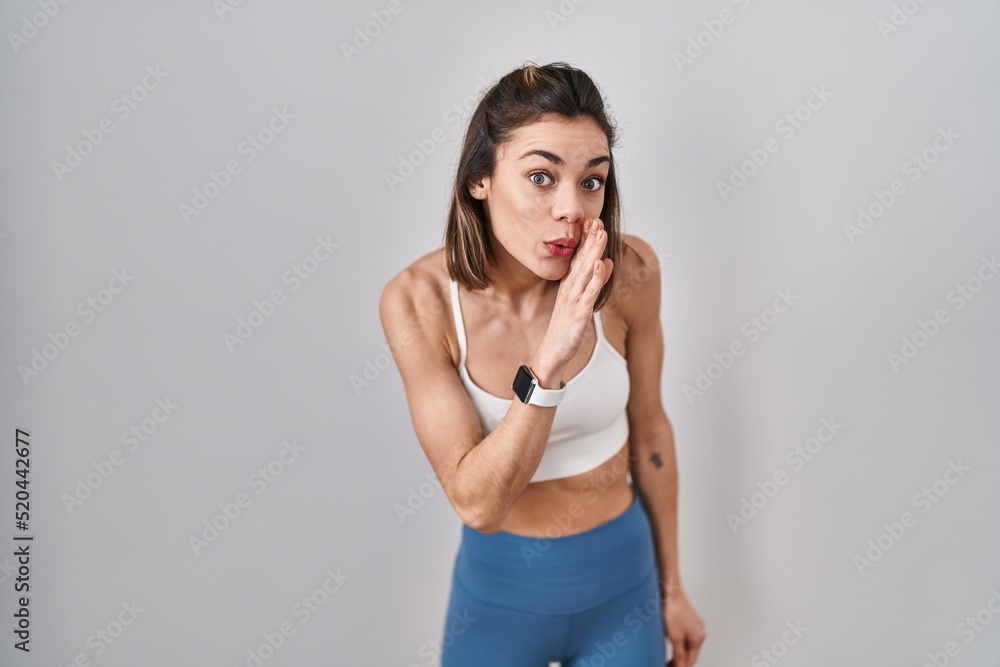 Hispanic woman wearing sportswear over isolated background hand on mouth telling secret rumor, whispering malicious talk conversation Hispanic woman wearing sportswear over isolated background hand on mouth telling secret rumor, whispering malicious talk conversation