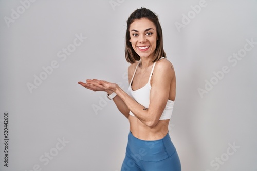 Hispanic woman wearing sportswear over isolated background pointing aside with hands open palms showing copy space, presenting advertisement smiling excited happy