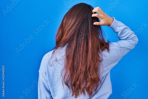 Hispanic young woman standing over blue background backwards thinking about doubt with hand on head