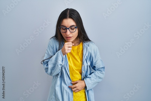 Young hispanic woman standing over blue background feeling unwell and coughing as symptom for cold or bronchitis. health care concept. © Krakenimages.com