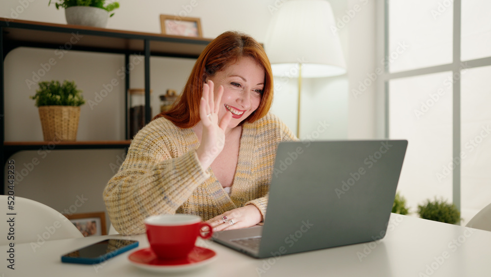 Fototapeta premium Young redhead woman having video call sitting on table at home