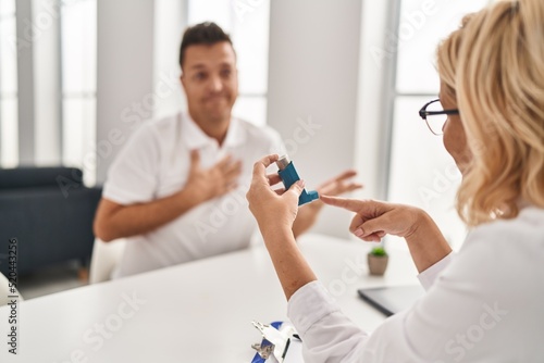 Middle age man and woman doctor and patient holding inhaler having medical consultation at clinic