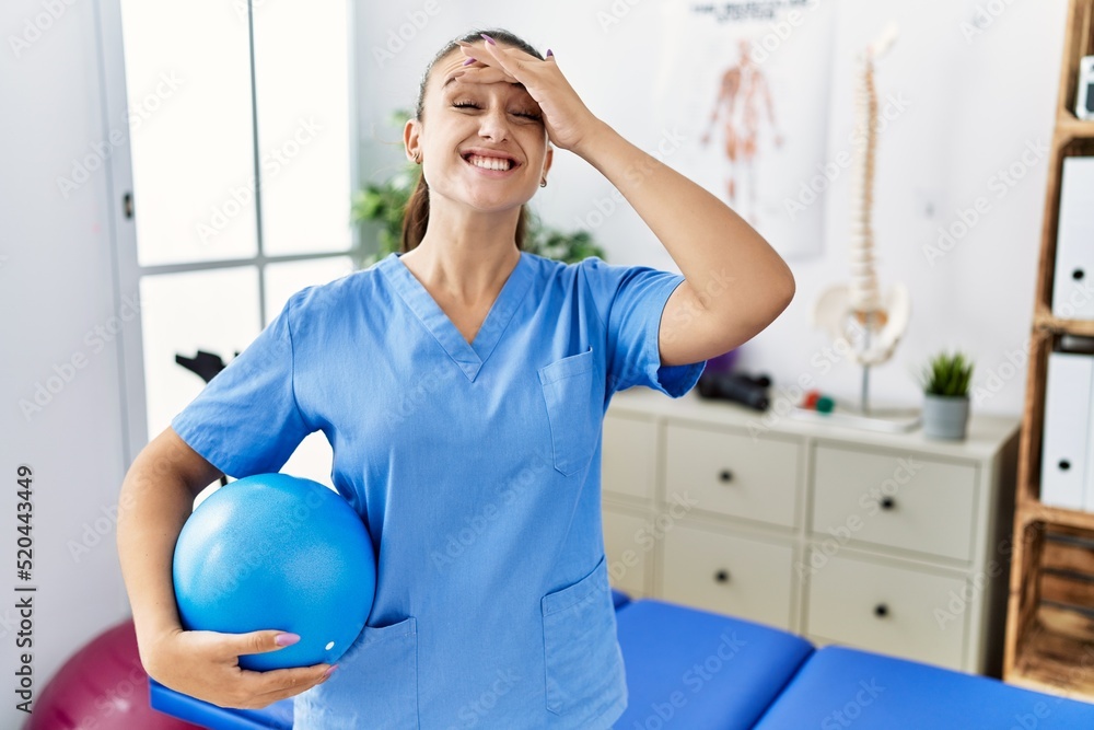Young physiotherapist woman holding pilates ball at medical clinic stressed and frustrated with hand on head, surprised and angry face Young physiotherapist woman holding pilates ball at medical clinic stressed and frustrated with hand on head, surprised and angry face