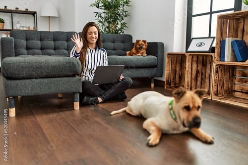 Sticker Young hispanic woman having video call sitting on floor with dogs at home
