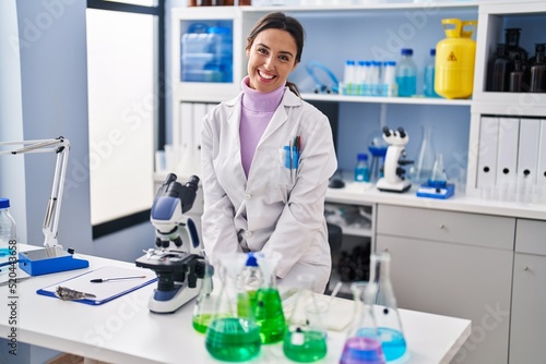Young brunette woman working at scientist laboratory looking positive and happy standing and smiling with a confident smile showing teeth