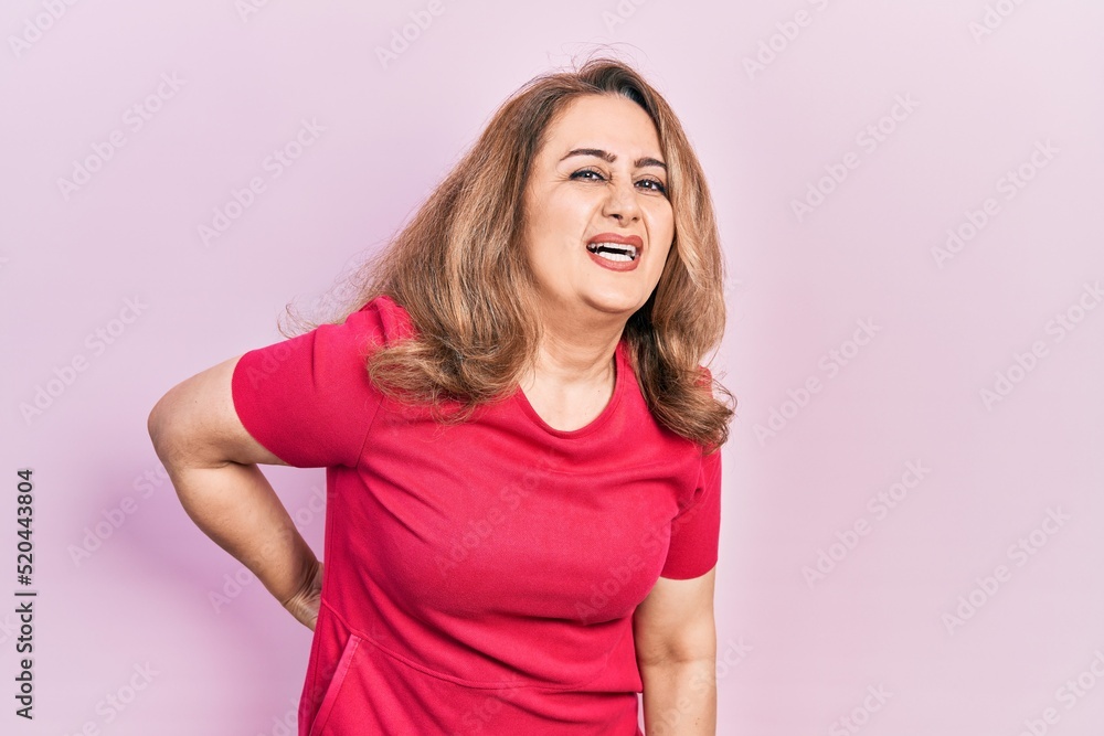 Middle age caucasian woman wearing casual clothes suffering of backache, touching back with hand, muscular pain Middle age caucasian woman wearing casual clothes suffering of backache, touching back with hand, muscular pain