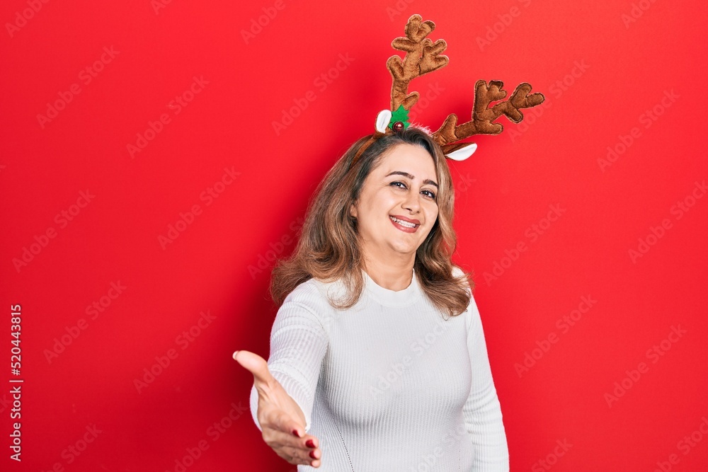 Middle age caucasian woman wearing cute christmas reindeer horns smiling friendly offering handshake as greeting and welcoming. successful business. Middle age caucasian woman wearing cute christmas reindeer horns smiling friendly offering handshake as greeting and welcoming. successful business.