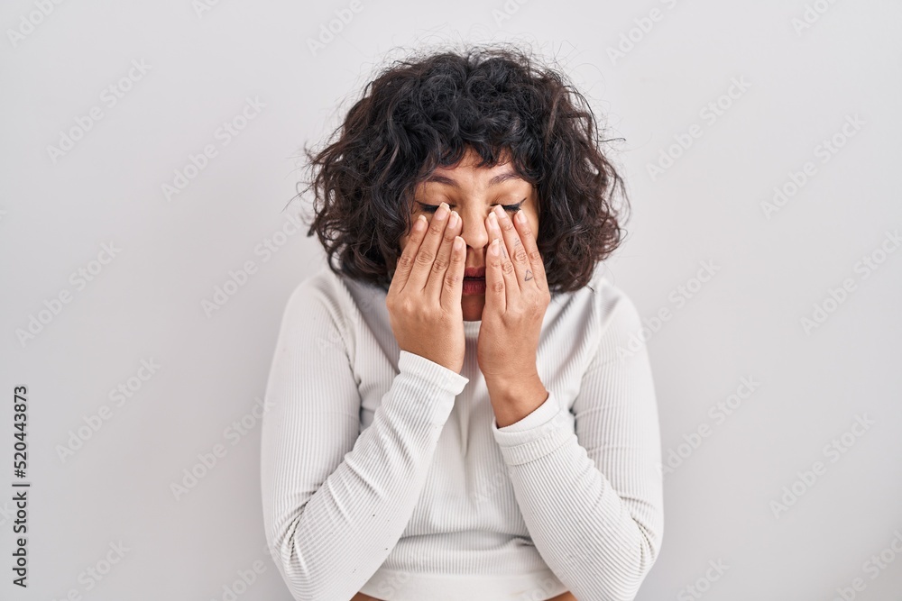 Hispanic woman with curly hair standing over isolated background rubbing eyes for fatigue and headache, sleepy and tired expression. vision problem Hispanic woman with curly hair standing over isolated background rubbing eyes for fatigue and headache, sleepy and tired expression. vision problem