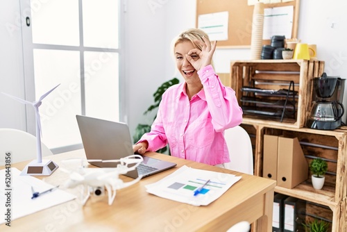 Young caucasian woman working at the office doing ok gesture with hand smiling, eye looking through fingers with happy face.
