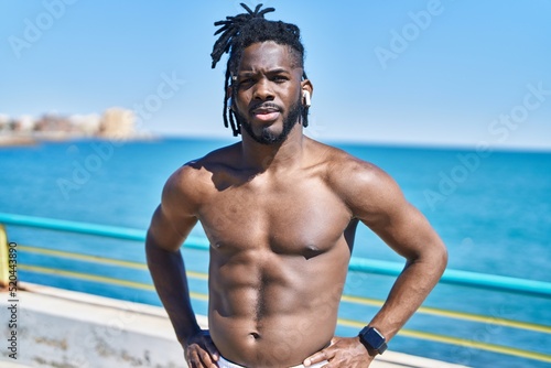 African american woman shirtless listening to music with serious expression at seaside