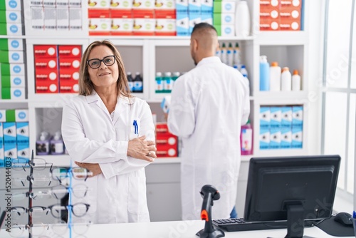 Man and woman pharmacist standing with arms crossed gesture at pharmacy