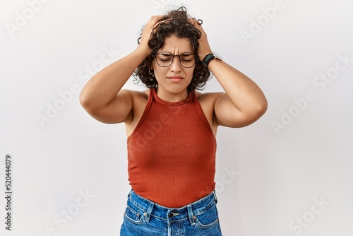 Young hispanic woman wearing glasses standing over isolated background suffering from headache desperate and stressed because pain and migraine. hands on head.