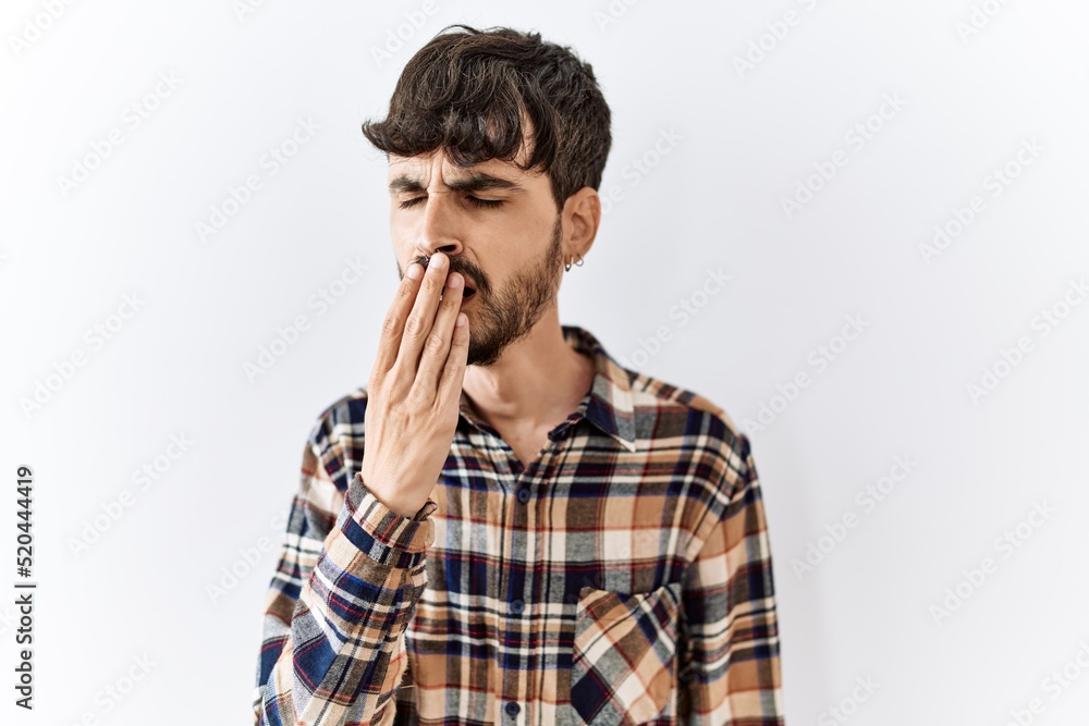 Hispanic man with beard standing over isolated background bored yawning tired covering mouth with hand. restless and sleepiness. Hispanic man with beard standing over isolated background bored yawning tired covering mouth with hand. restless and sleepiness.