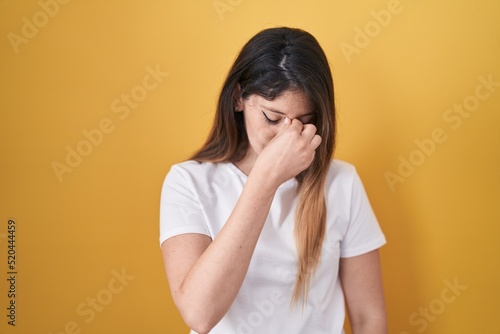 Young brunette woman standing over yellow background tired rubbing nose and eyes feeling fatigue and headache. stress and frustration concept. © Krakenimages.com