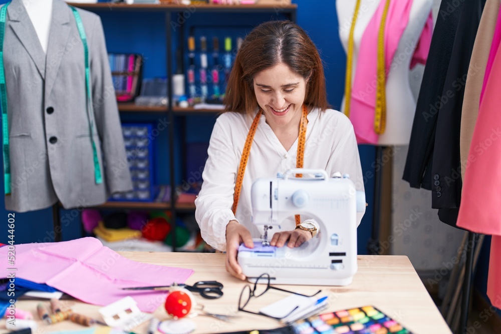 Fototapeta premium Young woman tailor smiling confident using sewing machine at sewing studio
